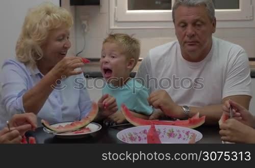 Grandmother feeding a little grandchild with watermelon in playful manner