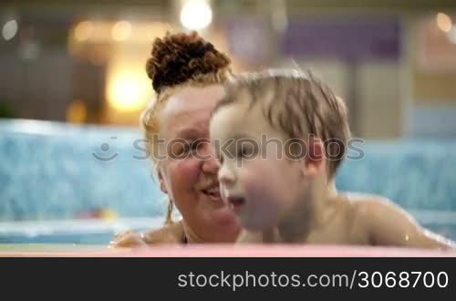 Grandmother helping her grandson to jump in the swimming pool, boy holding floatation devices