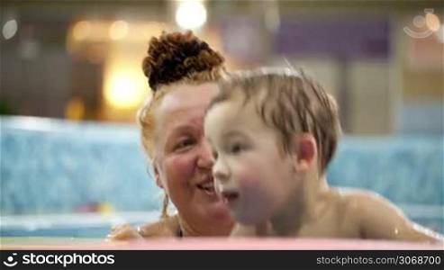 Grandmother helping her grandson to jump in the swimming pool, boy holding floatation devices