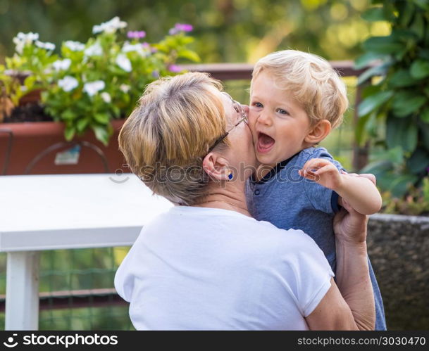 Grandmother hugs and gently kisses her grandchild in garden, natural light.