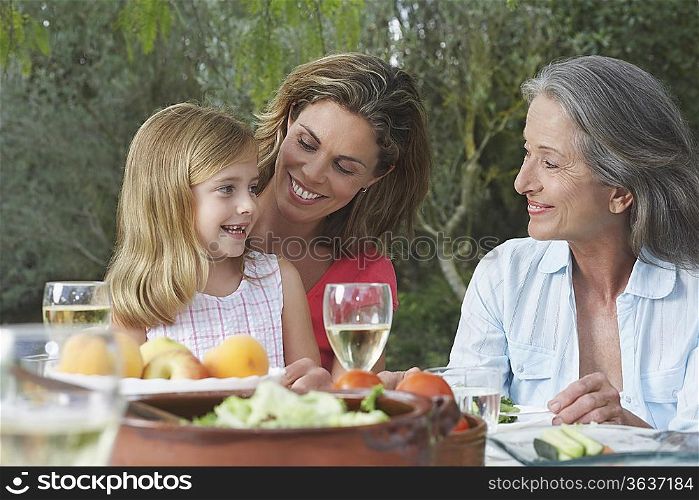 Grandmother, mother and daughter (5-6) sitting at table in garden
