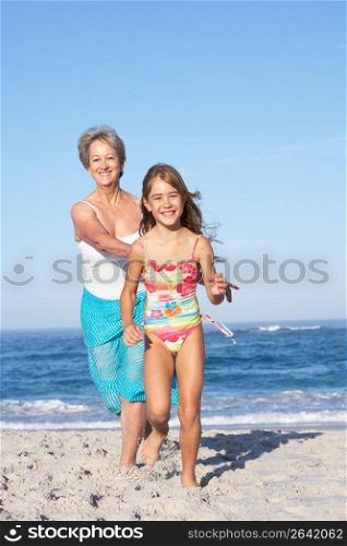 Grandmother Running With Granddaughter Along Sandy Beach