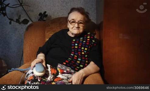 Grandmother sitting in the armchair with her hand on the phone. She waiting for a call. Problem of loneliness in the old age