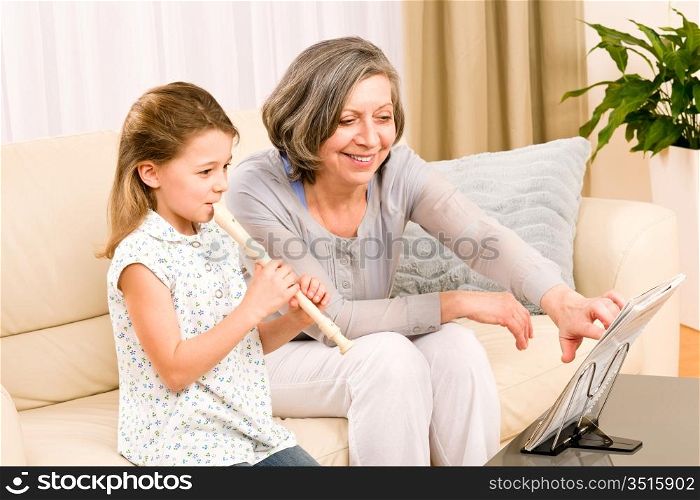 Grandmother teach young girl to play flute happy sitting on sofa