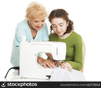 Grandmother teaching her teen granddaughter to use a sewing machine. Isolated on white.