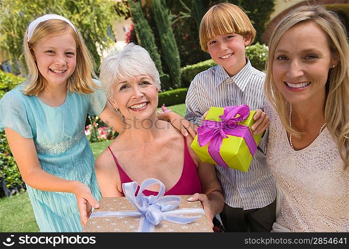 Grandmother with daughter and grandchildren in garden holding birthday present