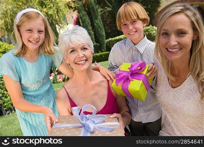 Grandmother with daughter and grandchildren in garden holding birthday present