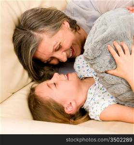 Grandmother with granddaughter hugging smiling together lying on sofa