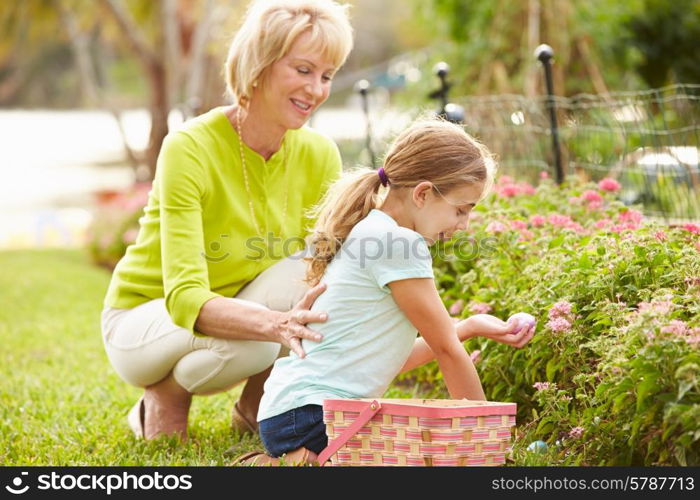 Grandmother With Granddaughter On Easter Egg Hunt In Garden