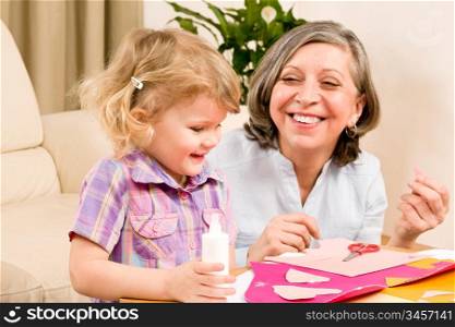Grandmother with granddaughter playing together glue hearts on paper