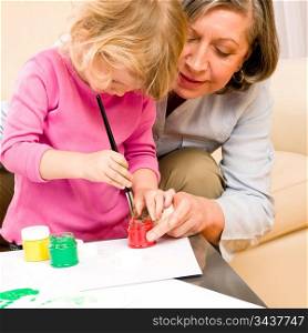 Grandmother with granddaughter playing together paint handprints on paper