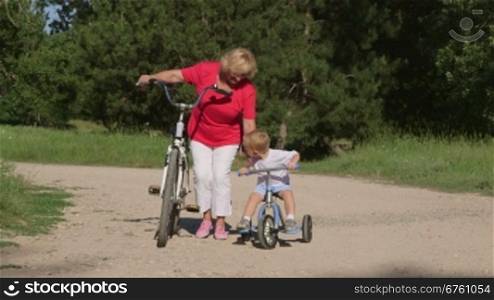 Grandmother with grandson riding bicycles in the summer park