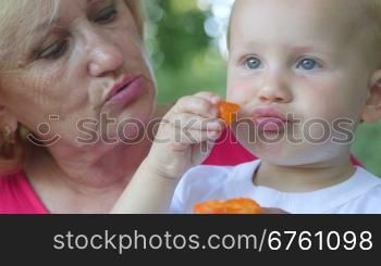 Grandmother with her grandchild eating apricot outdoors