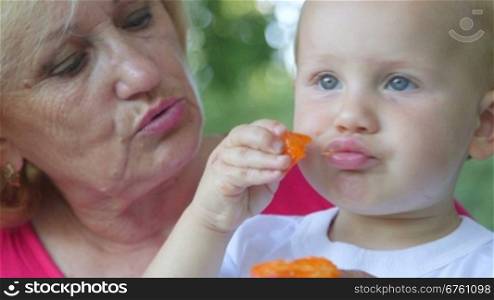Grandmother with her grandchild eating apricot outdoors