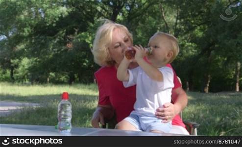 Grandmother with her grandson in the park, child drinking juice