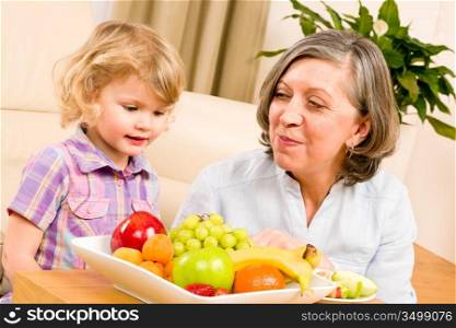 Grandmother with little granddaughter eating fruit happy together at home