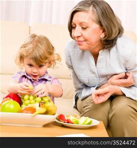 Grandmother with little granddaughter eating fruit happy together at home