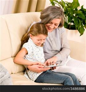 Grandmother with young girl use touch screen tablet computer smiling