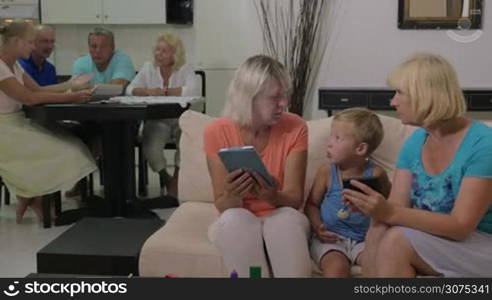 Grandmothers and grandson at home. One woman showing child something on mobile phone while another using tablet computer