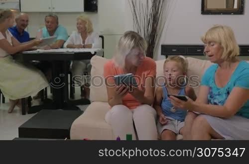 Grandmothers and grandson at home. One woman showing child something on mobile phone while another using tablet computer