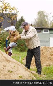 Grandpa helps grandson to get on a sand hill