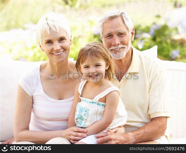 Grandparents And Granddaughter Relaxing In Garden