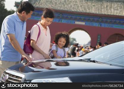 Grandparents and granddaughter standing next to the car and looking at the map