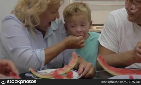 Grandparents and grandson eating ripe watermelon. Grandmother feeding little playful boy