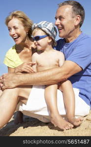 Grandparents And Grandson Sitting On Beach