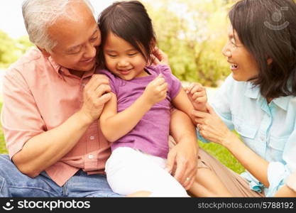 Grandparents Cuddling Granddaughter In Park