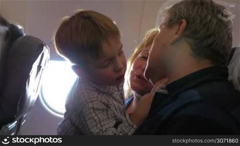 Grandparents traveling by plane with little grandchild. He examining grandfathers face, looking and pointing at his moles