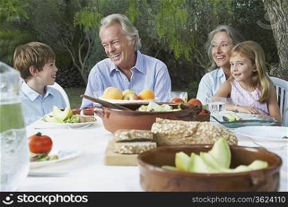 Grandparents with grandchildren (5-6) sitting at garden table