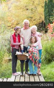 Grandparents With Grandchildren Carrying Picnic Basket By Autumn Woodland