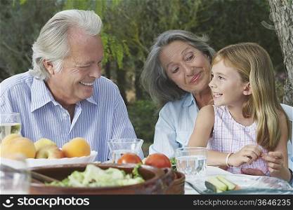 Grandparents with granddaughter (5-6) sitting at garden table