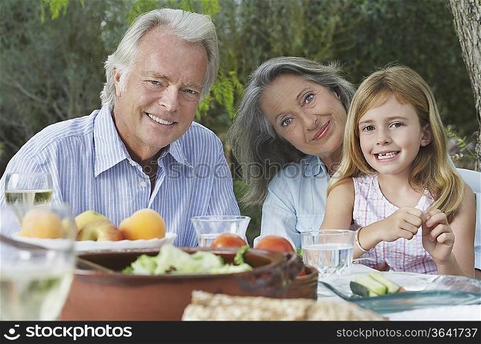 Grandparents with granddaughter (5-6) sitting at garden table, portrait