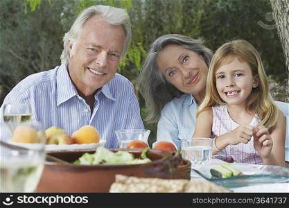 Grandparents with granddaughter (5-6) sitting at garden table, portrait