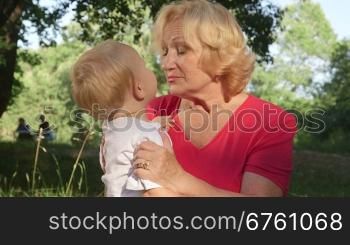 Grandson kissing her happy grandmother in summer park