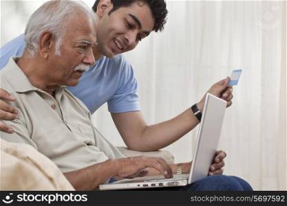 Grandson teaching grandfather how to operate laptop