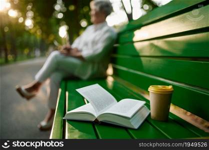 Granny drinks coffee on the bench in summer park. Aged people lifestyle. Pretty grandmother having fun outdoors, old female person on nature. Granny drinks coffee on the bench in summer park