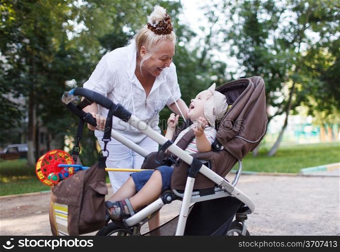 Granny playing with her grandson in a baby stroller in the yard.