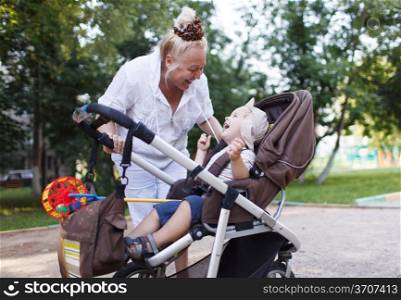Granny playing with her grandson in a baby stroller in the yard.