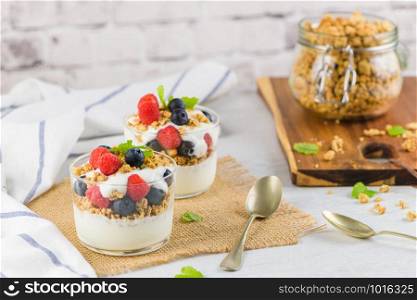 Granola blackberries and raspberries homemade yogurt in glass on light white wooden background. Healthy food concept.