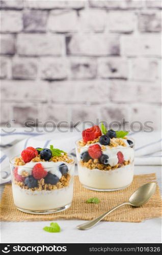 Granola blackberries and raspberries homemade yogurt in glass on light white wooden background. Healthy food concept.