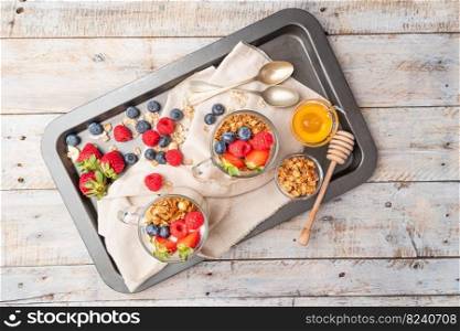 Granola with nuts, yogurt and red fruits berries in a jar. Breakfast parfait with muesli, yoghurt, red fruits berries and honey, white kitchen background.
