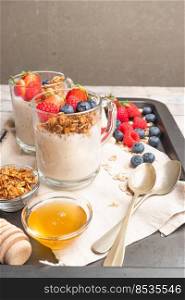 Granola with nuts, yogurt and red fruits berries in a jar. Breakfast parfait with muesli, yoghurt, red fruits berries and honey, white kitchen background.