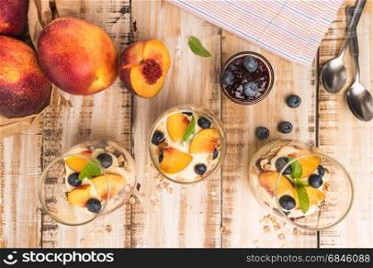 Granola with peaches, yogurt and blueberries on wooden table