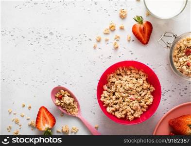 Granola with strawberry and milk in pink bowl plate on light background. Top view.