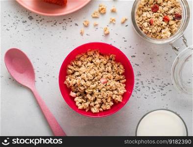 Granola with strawberry and milk in pink bowl plate on light kitchen background.
