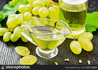 Grape oil in a gravy boat and a jar, berries of green grapes on the background of dark wooden board