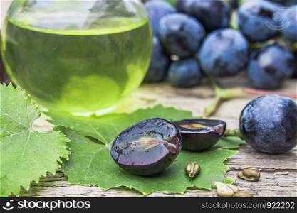 Grape seed oil in a glass bottle near blue grapes and green leaves on old wooden boards. Spa, bio, eco products concept.. Grape seed oil in a glass bottle near blue grapes and green leaves on old wooden boards. Spa, eco products concept.